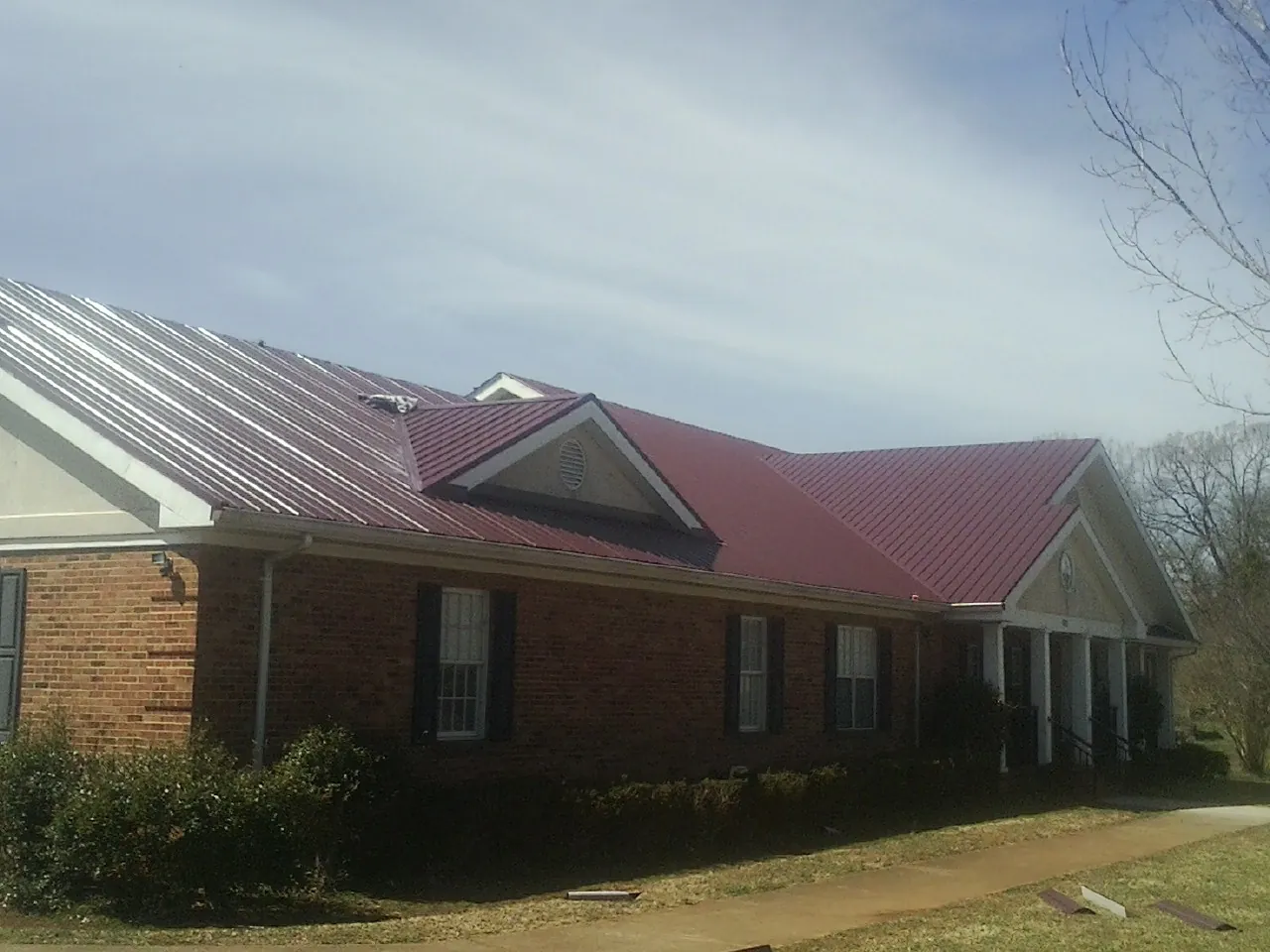 Red metal roof with gabled entries on a long brick building, from a Hail Damage Roof Repair job in Bremen