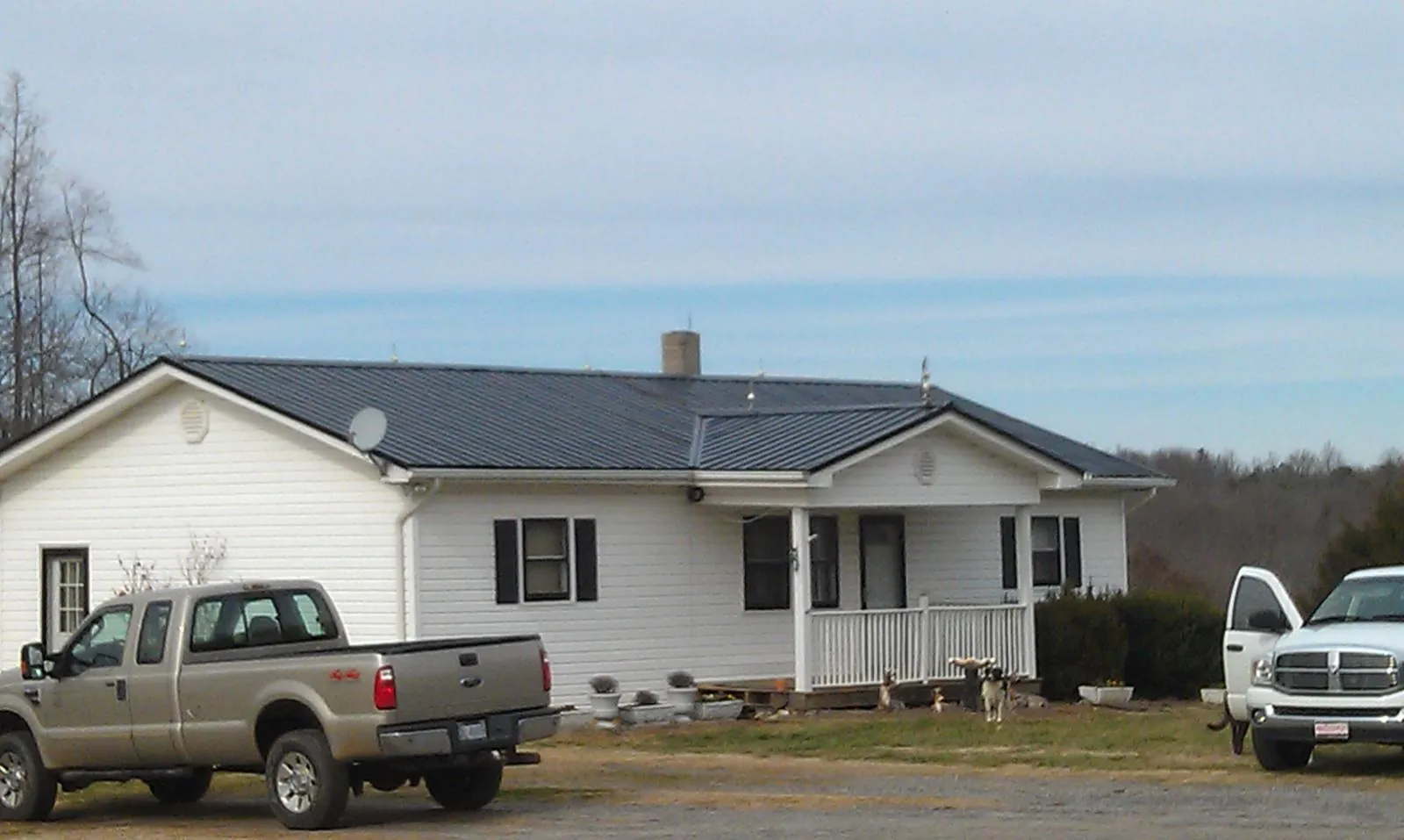 Finished dark metal roof on a white ranch home with work trucks parked in Bremen