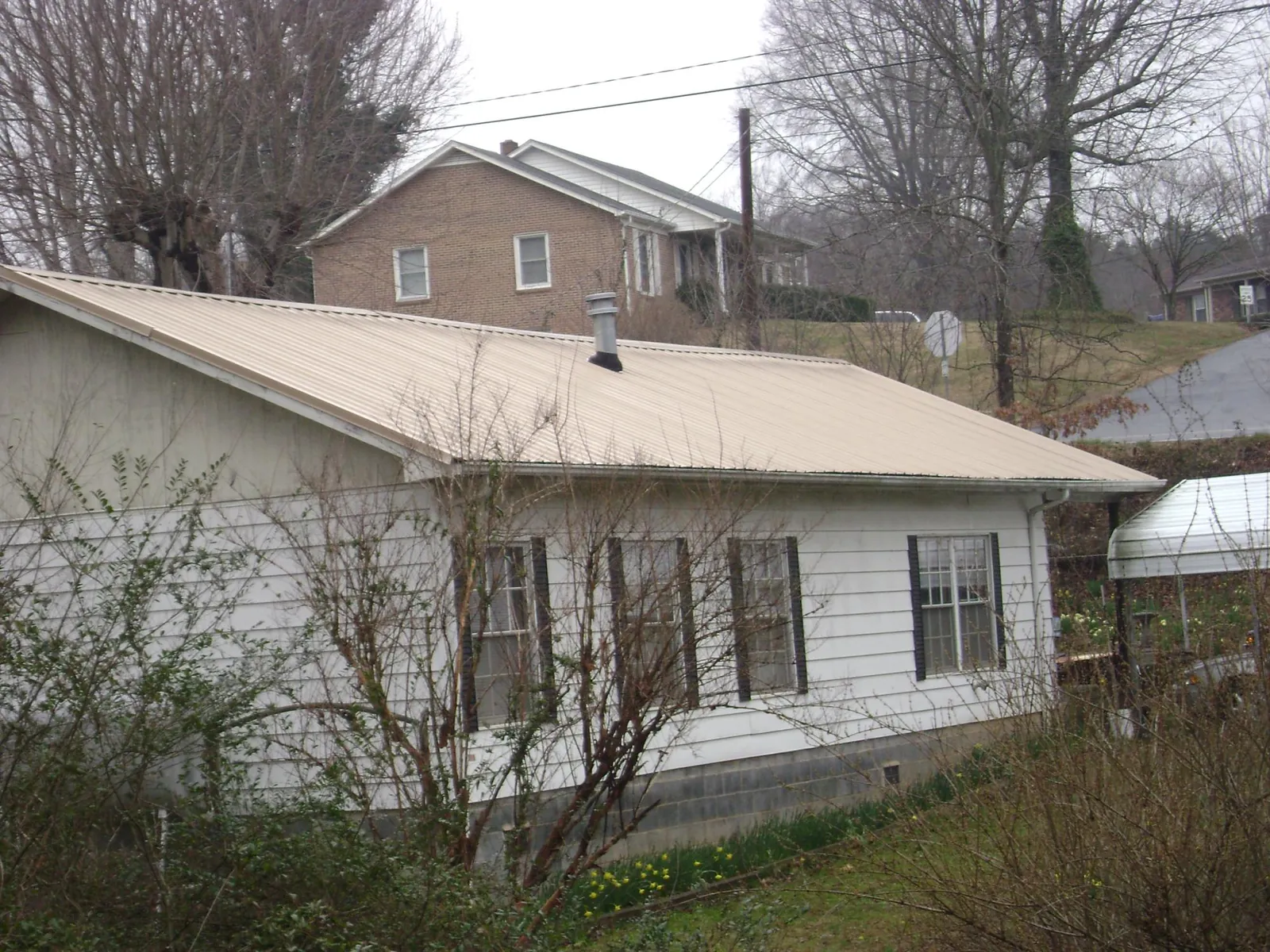 Tan metal roof on a white sided house set into a hillside — Commercial Roofing by Roofing Brothers in Bremen